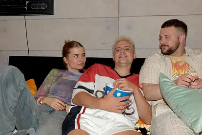 GZSZ-Szene: Johanna, Moritz und Jonas sitzen zusammen auf dem Sofa, Jonas und Johanna schauen sich verliebt an.