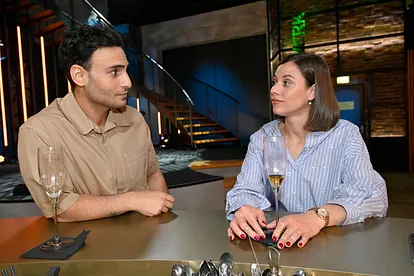 Nihat und Matilda sitzen mit einem Glas Champagner an der Bar und schauen sich zufrieden an.