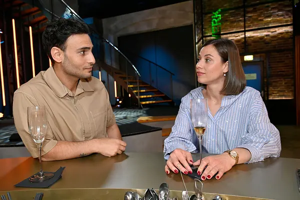 Nihat und Matilda sitzen mit einem Glas Champagner an der Bar und schauen sich zufrieden an.