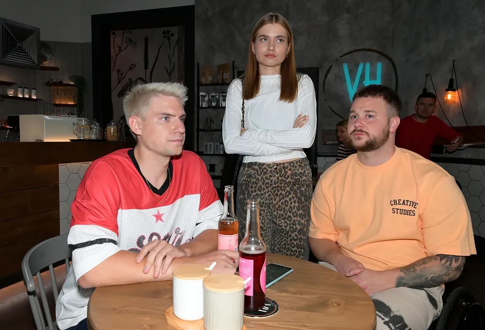Jonas und Moritz sitzen, Johanna hat die Arme verschränkt und schaut genervt.