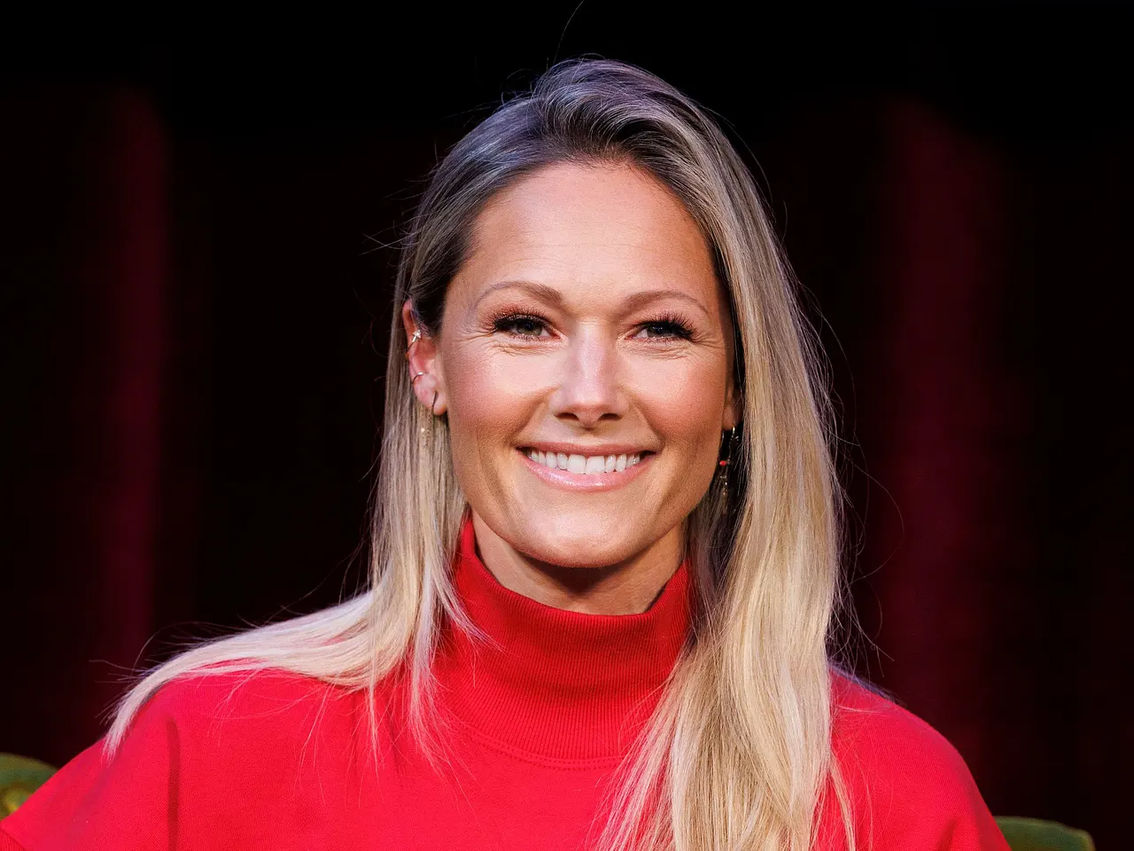 Helene Fischer sitzt in einem roten Pulli und strahlt in die Kamera. - Foto: IMAGO / Panama Pictures Helene Fischer sitzt in einem roten Pulli und strahlt in die Kamera.