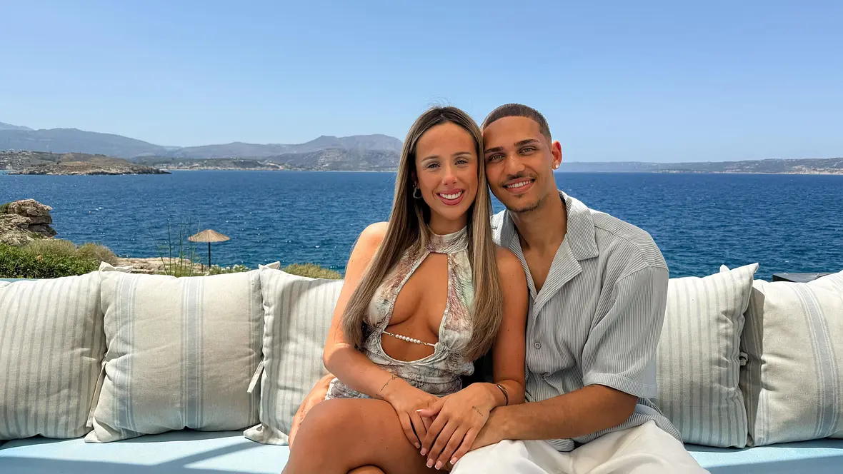 Ein Paar sitzt eng beieinander auf einer Couch vor einem Infinity-Pool mit weiter Aussicht auf das Meer.