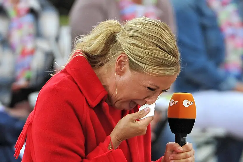 Andrea Kiewel, ganz in Rot gekleidet, weint auf der Bühne des ZDF-"Fernsehgarten" und drückt sich ein Taschentuch ins Gesicht. 