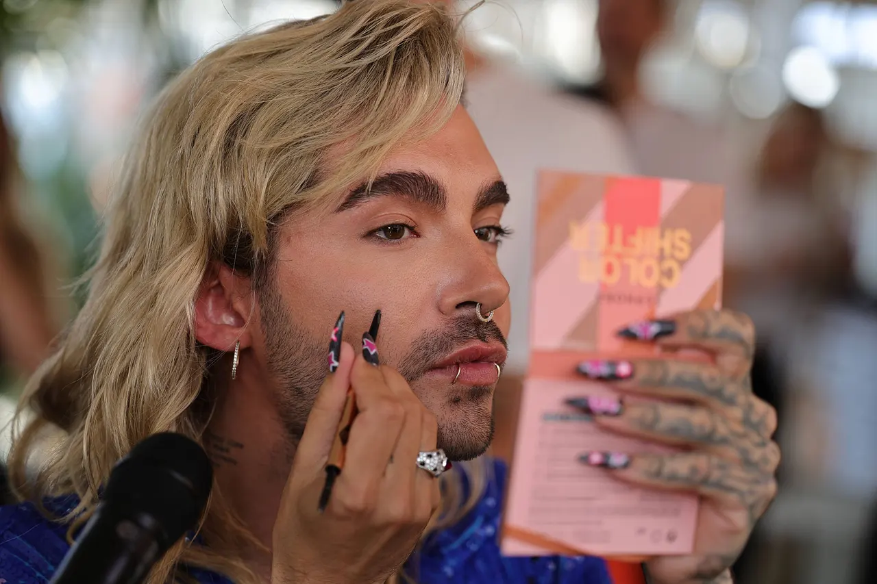 Bill Kaulitz schaut angestrengt in einen Handspiegel, während er sich stylt.  - Foto: IMAGO / Uwe Erensmann