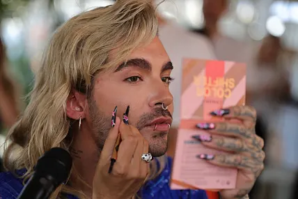Bill Kaulitz schaut angestrengt in einen Handspiegel, während er sich stylt. 