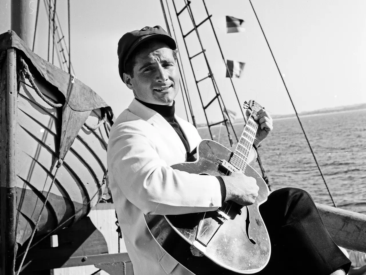 Zumindest aus Werbezwecken war Freddy Quinn häufiger auf Schiffen anzutreffen. Freddy Quinn sitzt an Bord eines Schiffes und hält eine Gitarre im Arm. Das Foto ist schwarz-weiß, Quinn lächelt in die Kamera. - Foto: IMAGO / United Archives