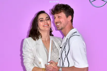 Renata Lusin und Valentin Lusin turteln in weißen Outfits vor pinkem Hintergrund. Liebevoll halten sich die Eltern der kleinen Stella an den Händen.