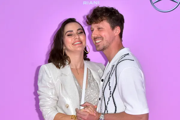 Renata Lusin und Valentin Lusin turteln in weißen Outfits vor pinkem Hintergrund. Liebevoll halten sich die Eltern der kleinen Stella an den Händen.