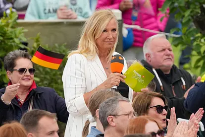 Andrea Kiewel im "ZDF-Fernsehgarten" am 18.05.2025 in Mainz. Sie steht im Publikum, hält ein Mikrofon und eine Moderationskarte.