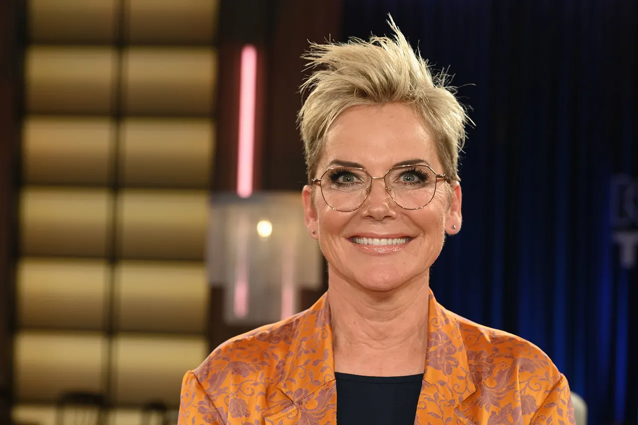 Inka Bause trägt eine Brille und lächelt in die Kamera.