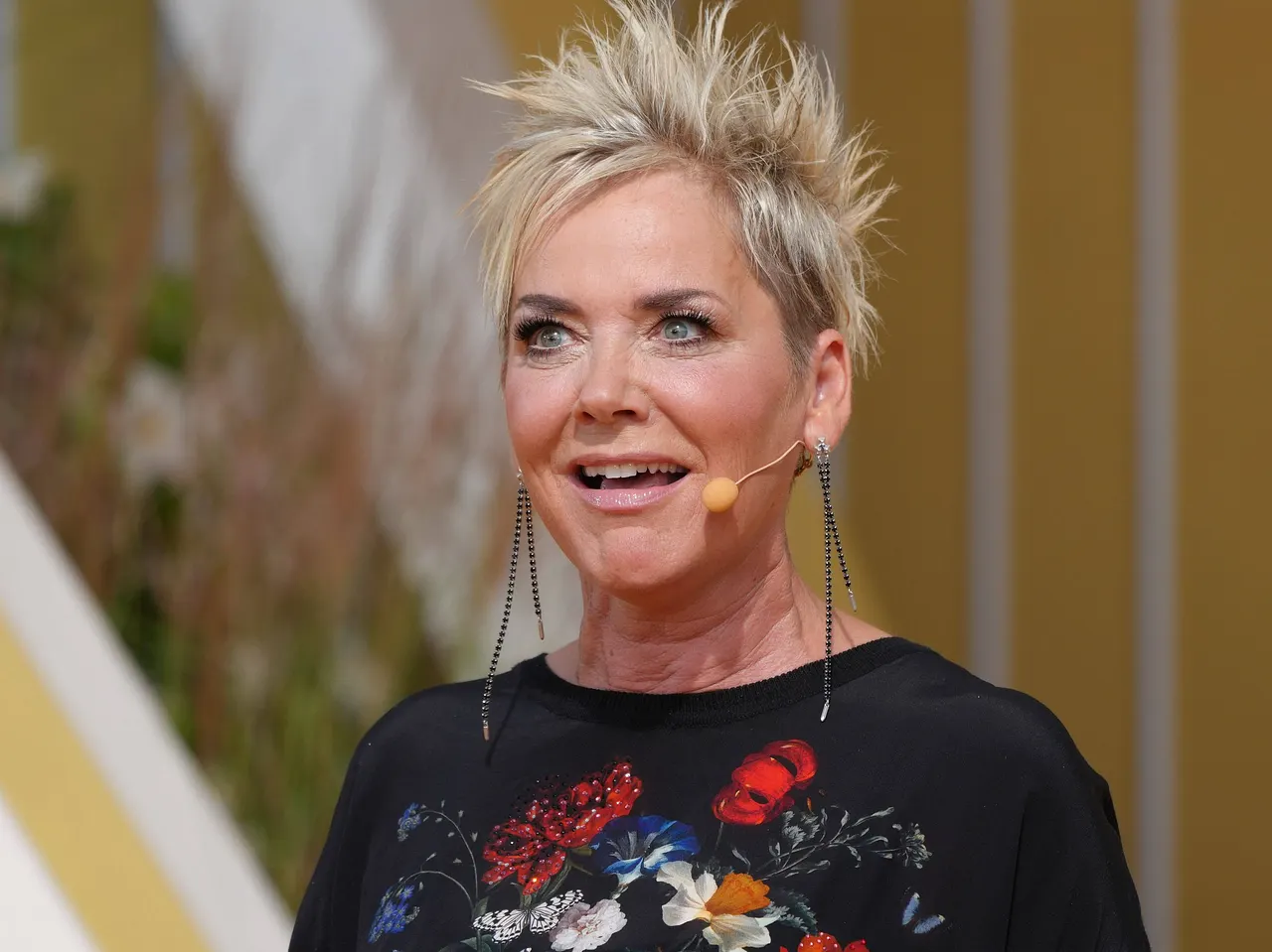 Inka Bause hat ein Mikro umgelegt und blickt lustig in die Ferne. - Foto: IMAGO / HOFER Inka Bause hat ein Mikro umgelegt und blickt lustig in die Ferne.