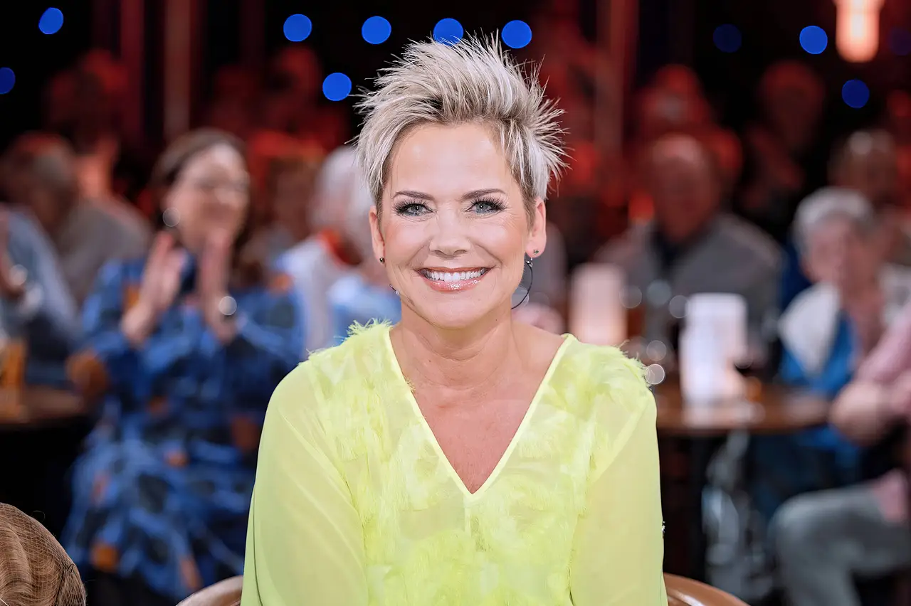 Inka Bause trägt eine gelbe Bluse und lächelt breit in die Kamera.