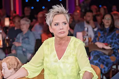 Inka Bause, hier in einer gelben Bluse und einer grünen Hose zu sehen, sieht sehr ernst aus. Sie trauert um ein Teammitglied.