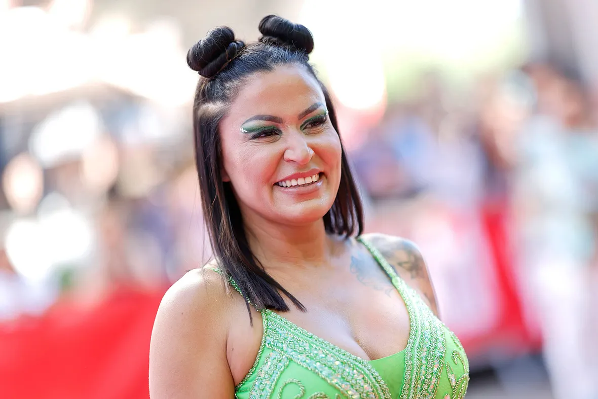 Jasmin Herren trägt zwei Space-Buns und grünen Lidschatten. Sie wird breit lächelnd von der Seite abgelichtet.