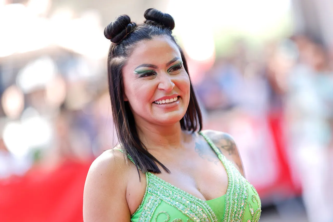 jasmin-herren-schulden-imago815818686 Jasmin Herren trägt zwei Space-Buns und grünen Lidschatten. Sie wird breit lächelnd von der Seite abgelichtet. - Foto: IMAGO / Panama Pictures
