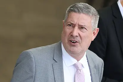 Joachim Lambi trägt ein weißes Hemd, eine rosa Krawatte und ein graues Jackett. 