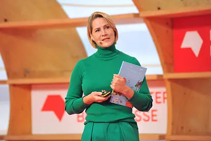 Judith Rakers hält ein Buch in der Hand und schaut ernst in die Ferne.