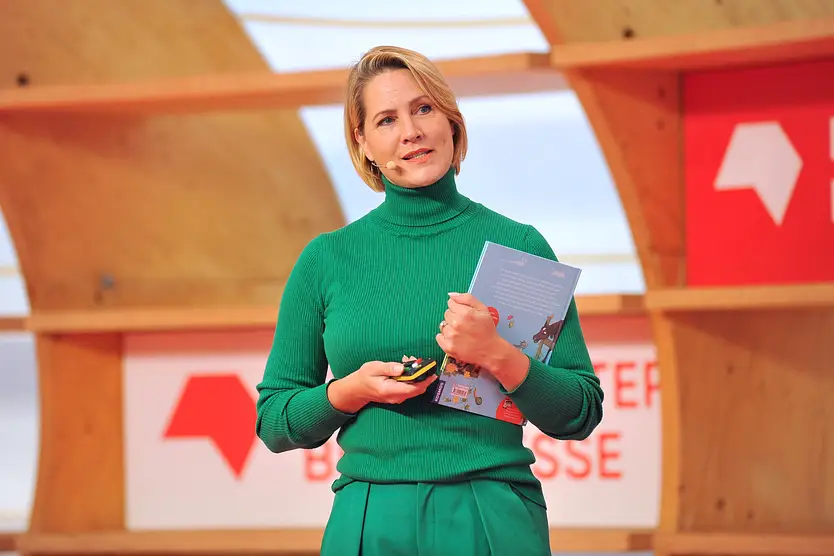 Judith Rakers hält ein Buch in der Hand und schaut ernst in die Ferne.