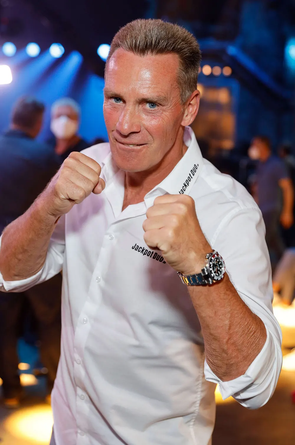 Jürgen Milski mit einem ernsten Gesichtsausdruck. Er hält seine Fäuste in die Höhe und täuscht einen Boxkampf vor. 