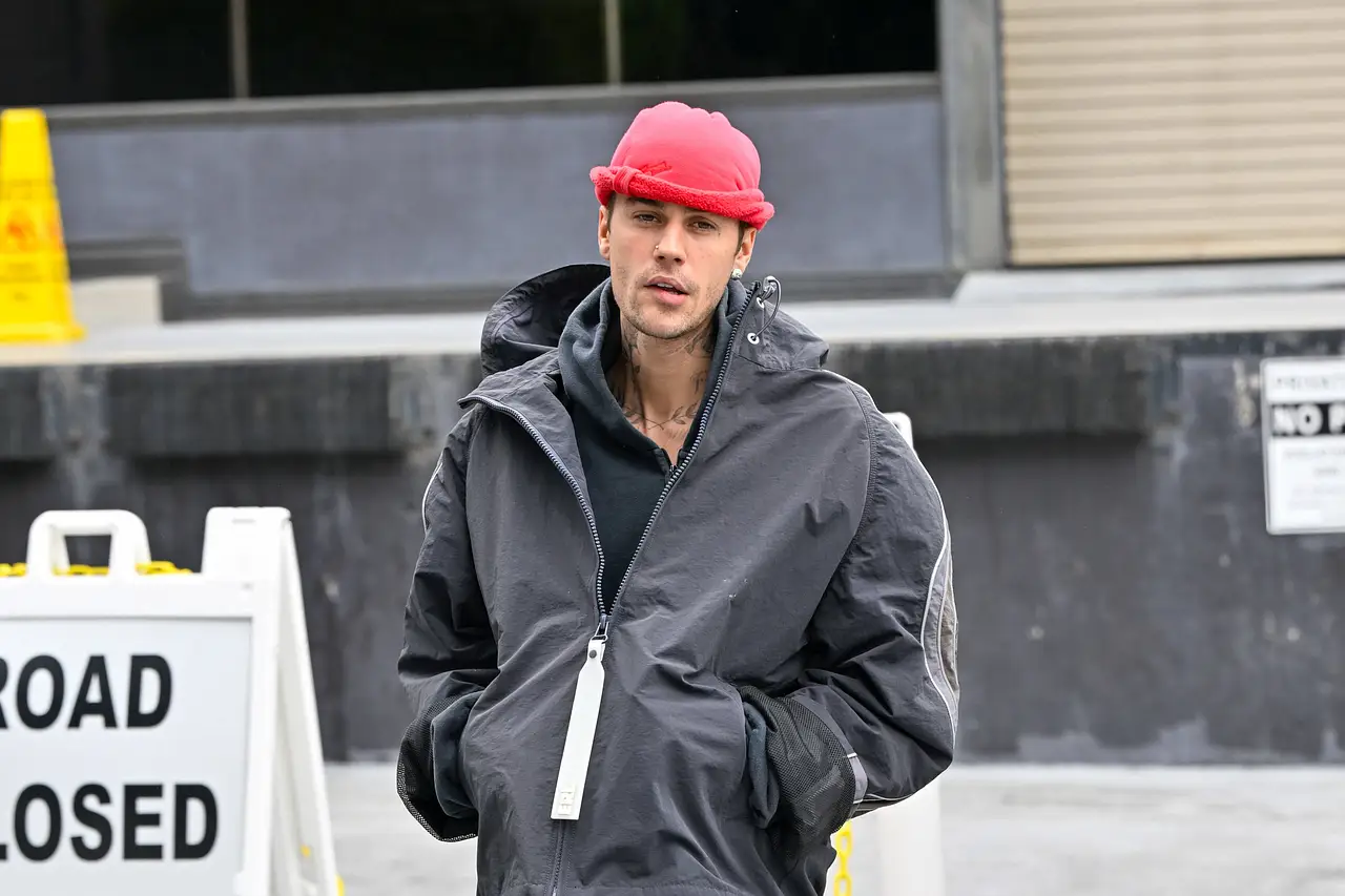 Justin Bieber trägt eine rote Mütze und eine schwarze Jacke, er die Hände in den Jackentaschen und schaut geradeaus.