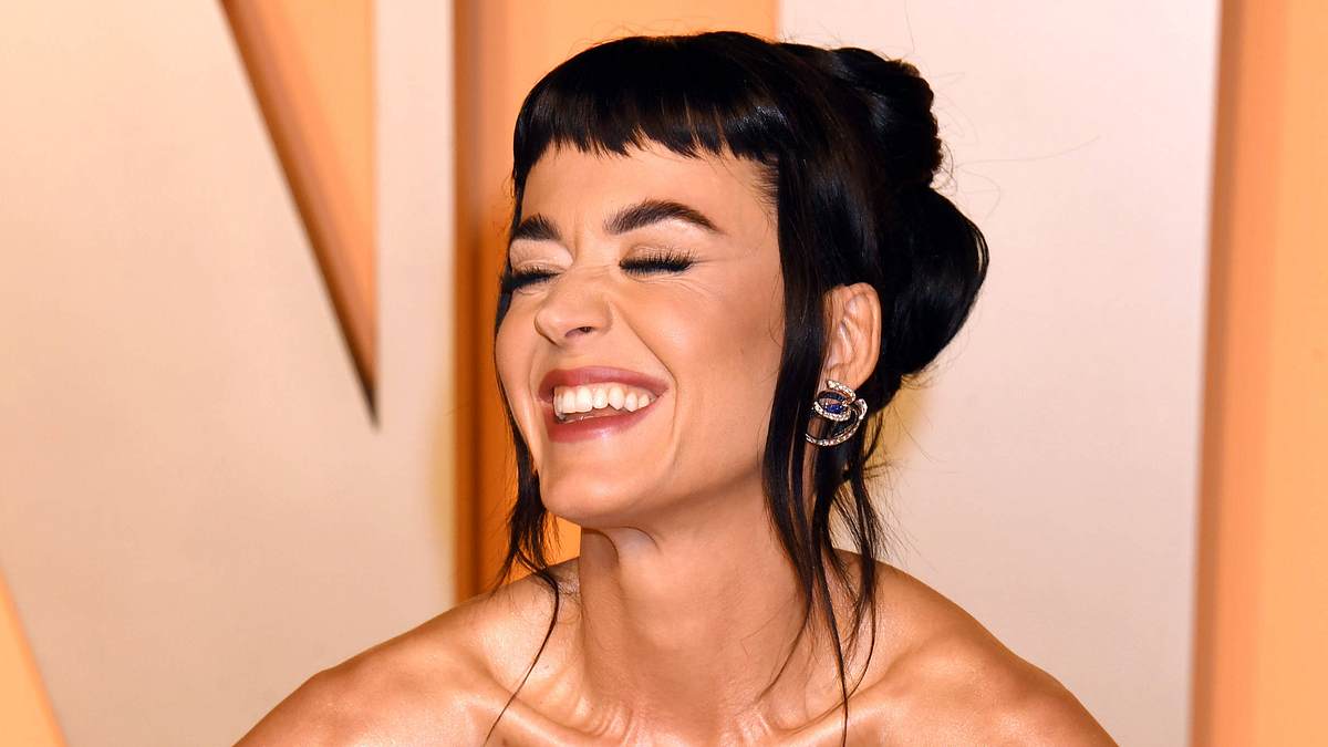 Katy Perry lächelt schräg an der Kamera vorbei und hat die Hände in die Hüfte gestemmt. Sie trägt ein goldenes Abendkleid und hat einen kurzen Pony