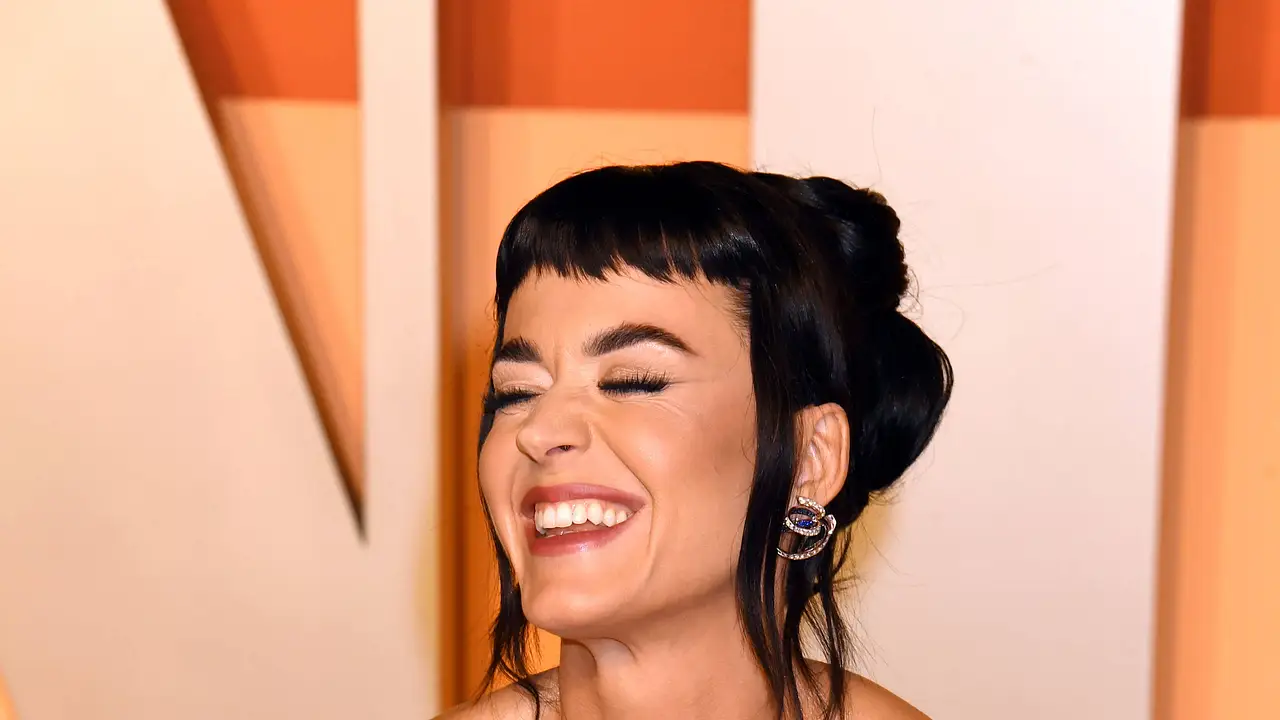 Katy Perry lächelt schräg an der Kamera vorbei und hat die Hände in die Hüfte gestemmt. Sie trägt ein goldenes Abendkleid und hat einen kurzen Pony