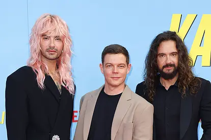Bill Kaulitz, Georg Listing und Tom Kaulitz schauen vor blauem Hintergrund ernst in die Kamera.