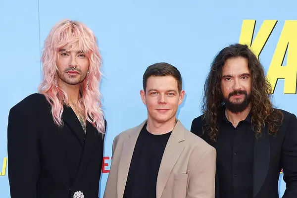 Bill Kaulitz, Georg Listing und Tom Kaulitz schauen vor blauem Hintergrund ernst in die Kamera. 