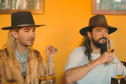 Bill Kaulitz und Tom Kaulitz sitzen mit Cowboyhüten an einem Tisch und trinken Alkohol.