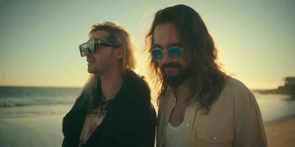 Bill und Tom Kaulitz in einer Szene ihrer Doku am Strand, beide tragen Sonnenbrillen und blicken ernst in die Ferne. Bill und Tom Kaulitz in einer Szene ihrer Doku am Strand, beide tragen Sonnenbrillen und blicken ernst in die Ferne.