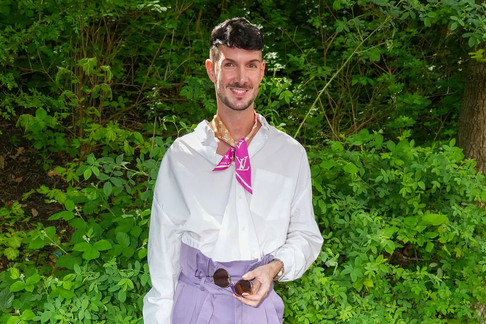 Kevin Schäfer trägt ein weißes Hemd und ein Louis Vuitton Tuch um seinen Hals. Er lächelt entspannt in die Kamera. Kevin Schäfer trägt ein weißes Hemd und ein Louis Vuitton Tuch um seinen Hals. Er lächelt entspannt in die Kamera.