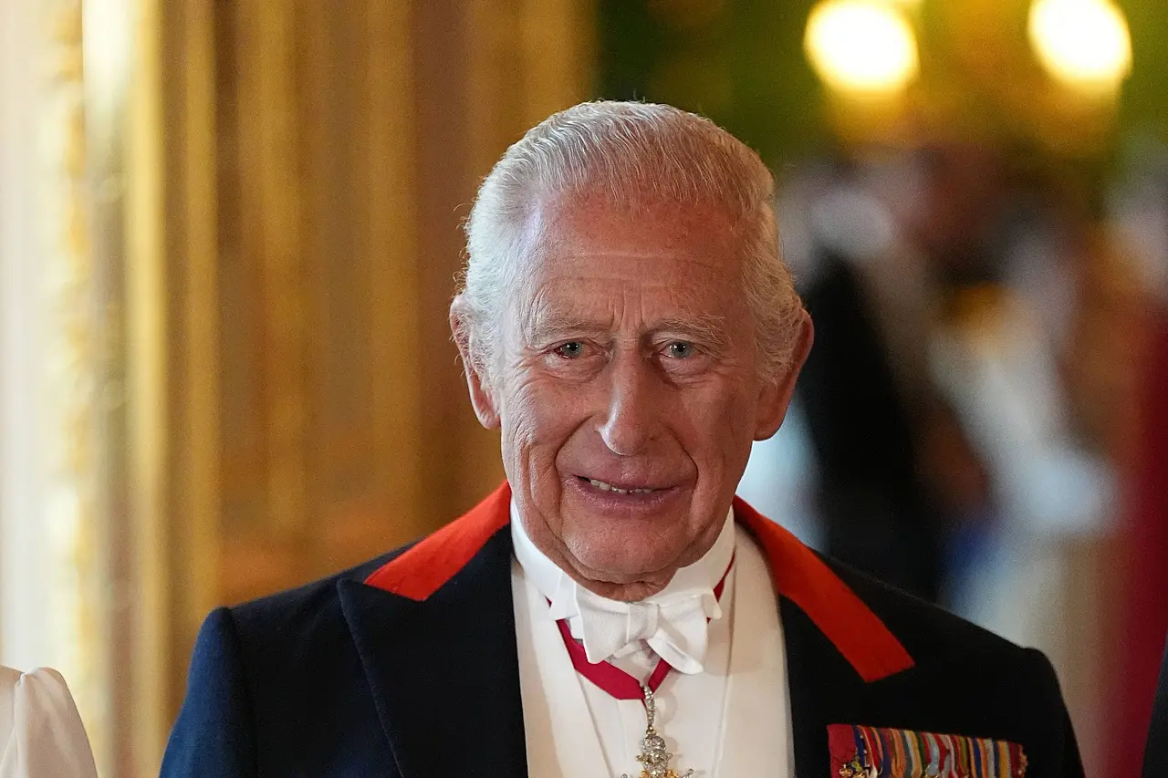 König Charles III. in einem Jackett voller Orden. Er lächelt und es ist leicht erkennbar, dass sein linkes Auge Blut unterlaufen ist. 