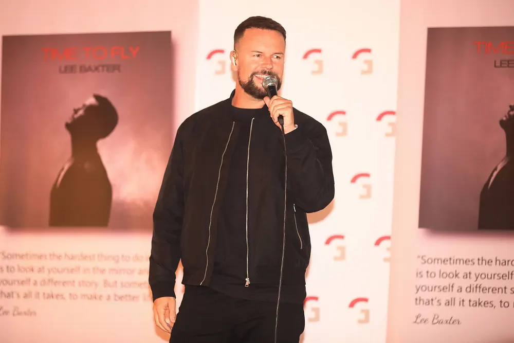 Lee Baxter lächelt und hält ein Mikrofon vor seinen Mund Lee Baxter lächelt und hält ein Mikrofon vor seinen Mund