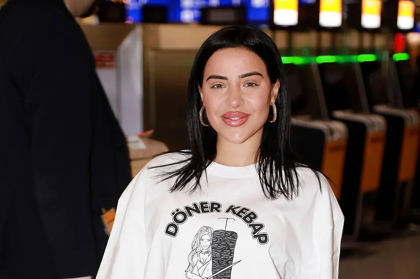 Leyla Heiter: Beauty-OP sorgt für Drama Leyla Heiter lächelt in die Kamera. Sie trägt pinken Lippenstift und einen weißen Pullover mit der Aufschrift "Döner Kebap"