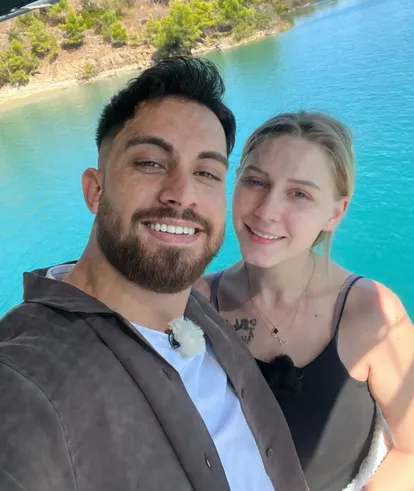 Loredana und Servet vor türkisblauem Wasser. Beide lächeln in die Kamera.