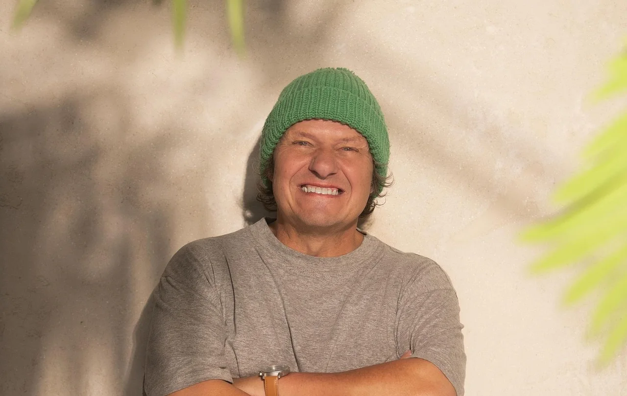 Manni Ludolf, hier mit einer grünen Mütze und einem grauen T-Shirt, lächelt breit in die Kamera. - Foto: Joyn / Michael de Boer