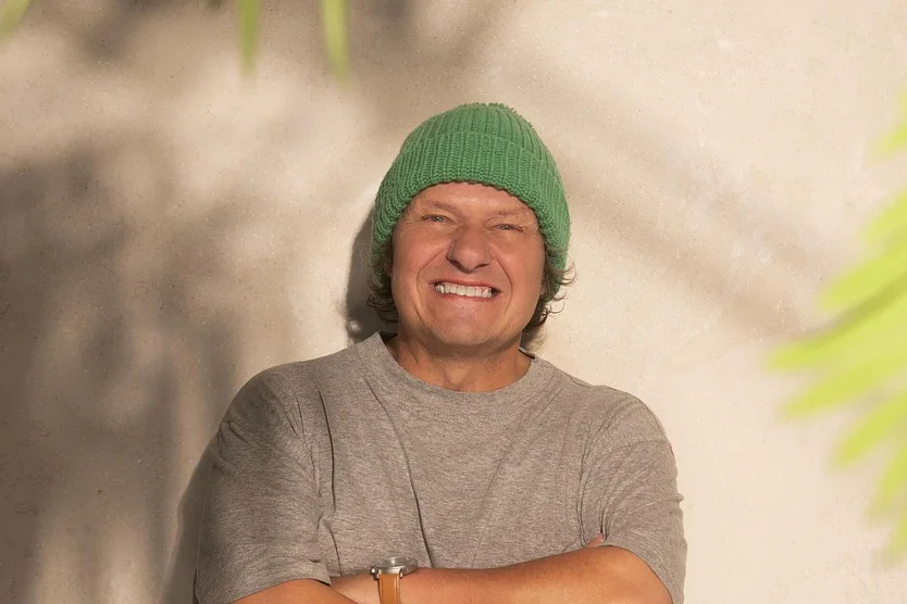 Manni Ludolf, hier mit einer grünen Mütze und einem grauen T-Shirt, lächelt breit in die Kamera.