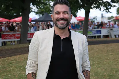 Marc Terenzi, hier in einem schwarzen Shirt und einem weißen Blazer zu sehen, strahlt glücklich in die Kamera.