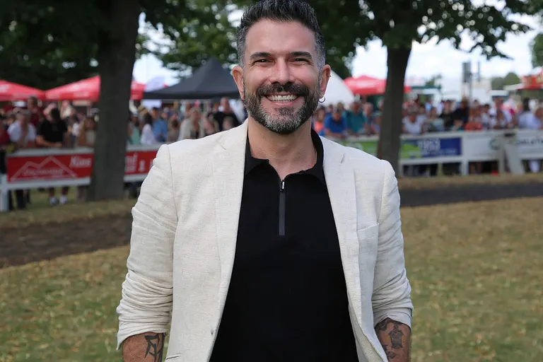 Marc Terenzi, hier in einem schwarzen Shirt und einem weißen Blazer zu sehen, strahlt glücklich in die Kamera.