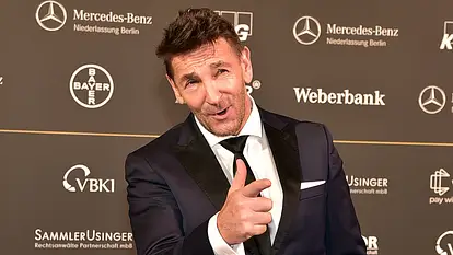 Mark Keller im Anzug zeigt einen Finger in die Kamera