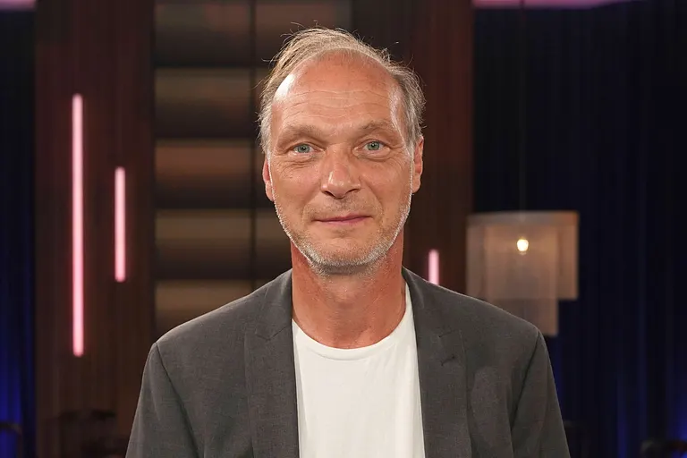 Martin Brambach bei der Aufzeichnung der WDR-Talkshow Kölner Treff am 16.08.2024 in weißem Shirt und grauem Sakko. 