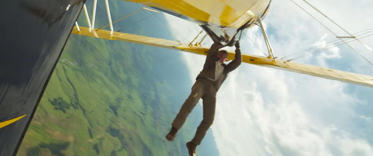 So kommt man schnell und günstig von A nach B: Tom Cruise in "Mission: Impossible 8". Tom Cruise hängt als Ethan Hunt an einem gelben Flugzeug, das kopfüber fliegt. - Foto: Paramount Pictures