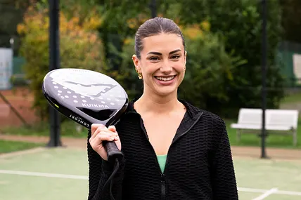 Kandidatin Lena posiert lächelnd mit einem Tennisschläger auf dem Spielfeld.
