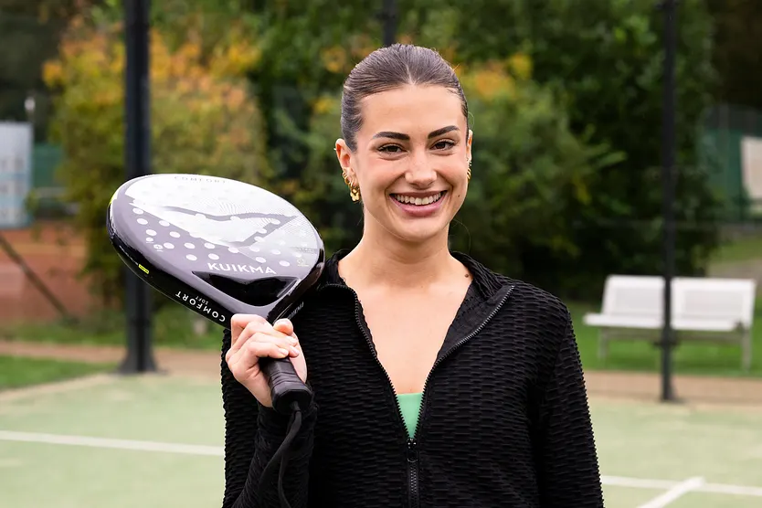 Kandidatin Lena posiert lächelnd mit einem Tennisschläger auf dem Spielfeld.
