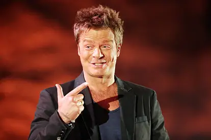 Oliver Geissen lächelt und hält zwei Finger in die Höhe.