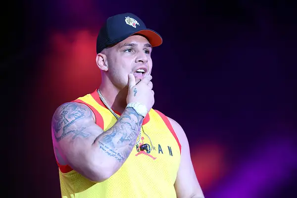 Pietro Lombardi steht im gelben Top und mit Kappe auf der Bühne und greift sich an den Mund. Sein Arm ist über und über tätowiert.