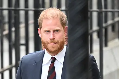 Prinz Harry trägt einen Anzug und streckt die Zunge leicht raus.