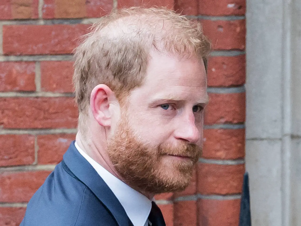 Prinz Harry trägt einen Anzug und wird in London mit ernster Miene von Fotografen abgelichtet.