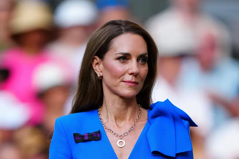 Prinzessin Kate trägt ein blaues Kleid und lächelt sanft. Sie wirkt in Gedanken verloren.