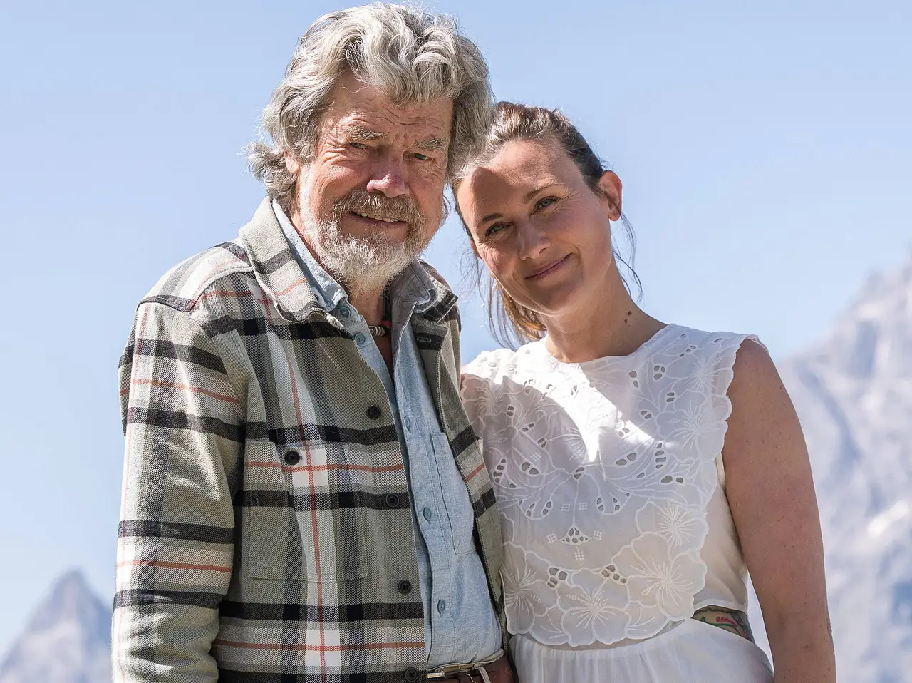 Reinhold Messner und seine Ehefrau Diane stehen lächelnd vor einer Bergkulisse in den Alpen